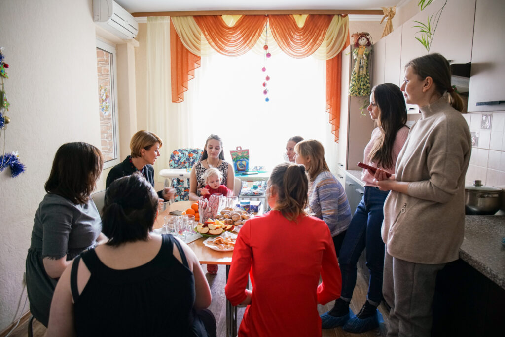 alyna Meeting with clients at a halfway house; several women and a baby gathered around the table of a kitchen